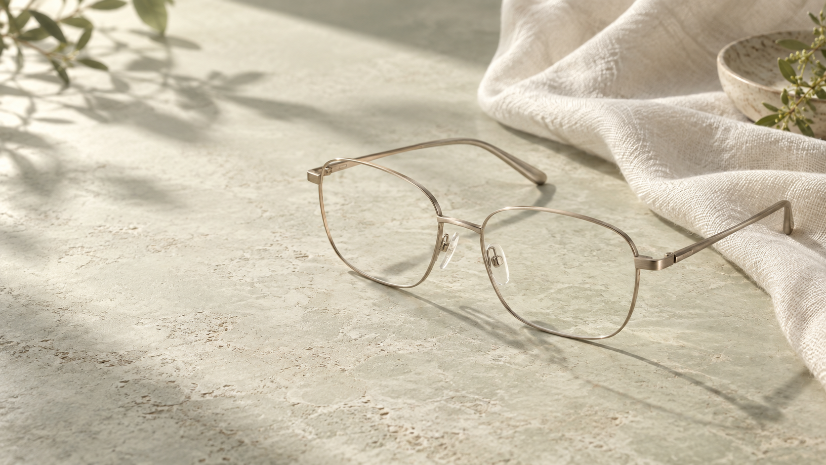Champagne titanium optical glasses with clear lenses on a pale stone surface